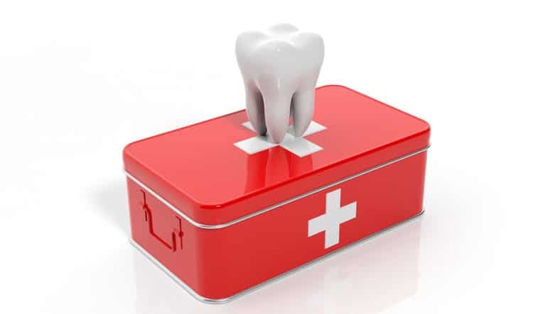 A white model of a molar tooth standing upright on a small, red first aid box with white crosses, symbolizing a dental emergency kit.