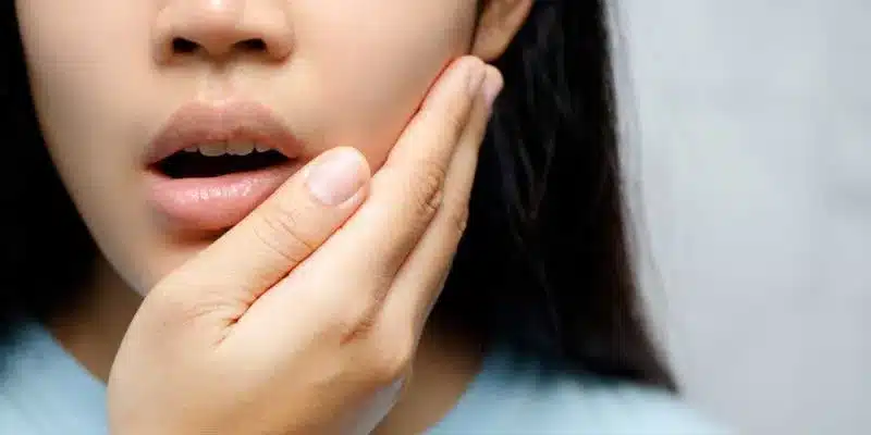 Woman holding her cheek with a concerned expression suggesting tooth pain